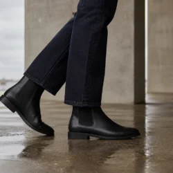 Kvinde i mørkeblå jeans og sorte Chelsea boots i en betonkolonnade efter regn