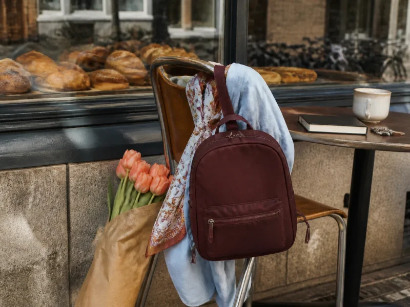 Bordeaux lille rygsæk på caféstol med blå skjorte, tørklæde og tulipaner