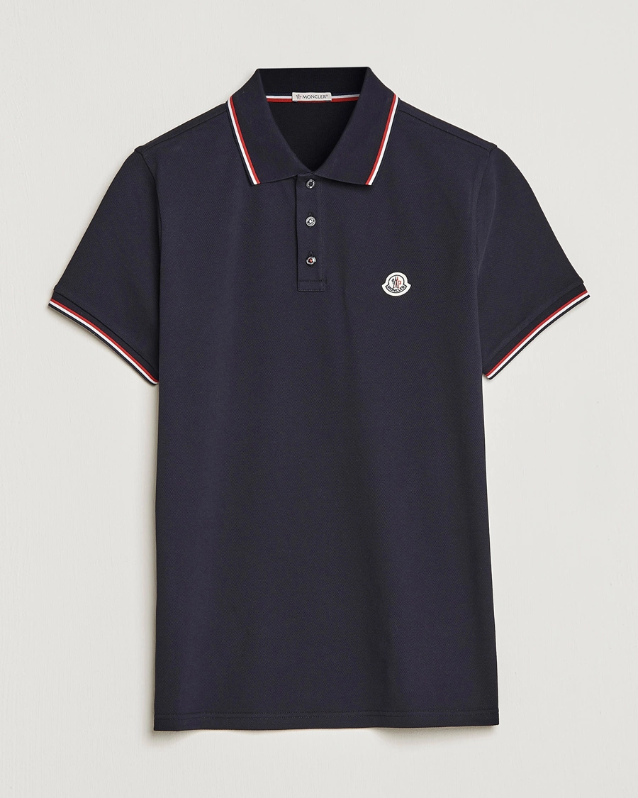 Elegant mørkeblå Moncler polo-shirt med karakteristiske røde og hvide striber på kraven og ærmerne, ideel for en tidløs herrestil.