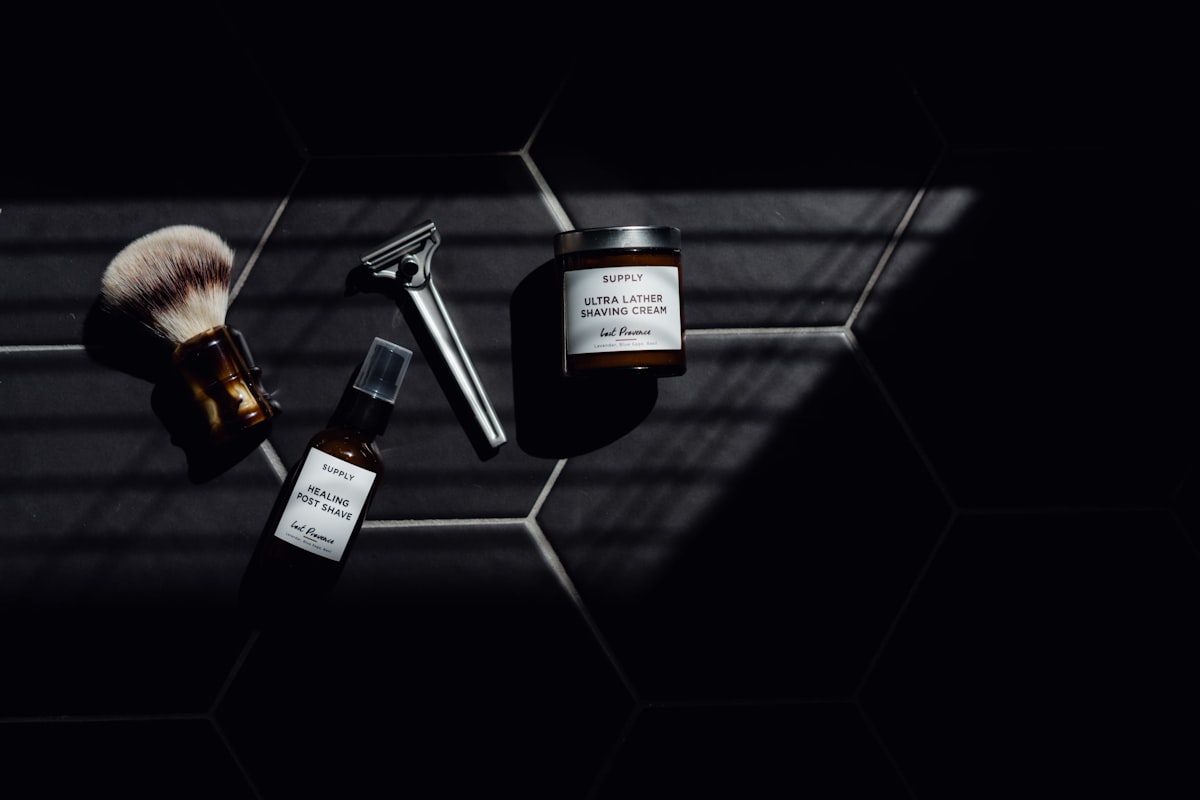 Barberkost, sikkerhedshøvl og aftershave-produkter på mørke fliser