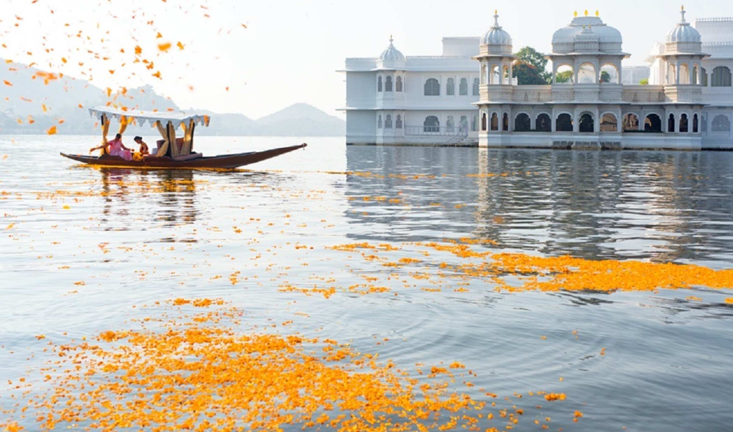 Traditionel båd med marigold-blomsterblade på Lake Pichola med Taj Lake Palace i morgenlys