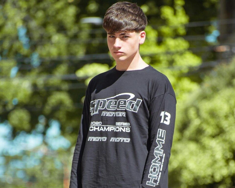Mand i grafisk sort sweatshirt og løse jeans på en grøn villavej