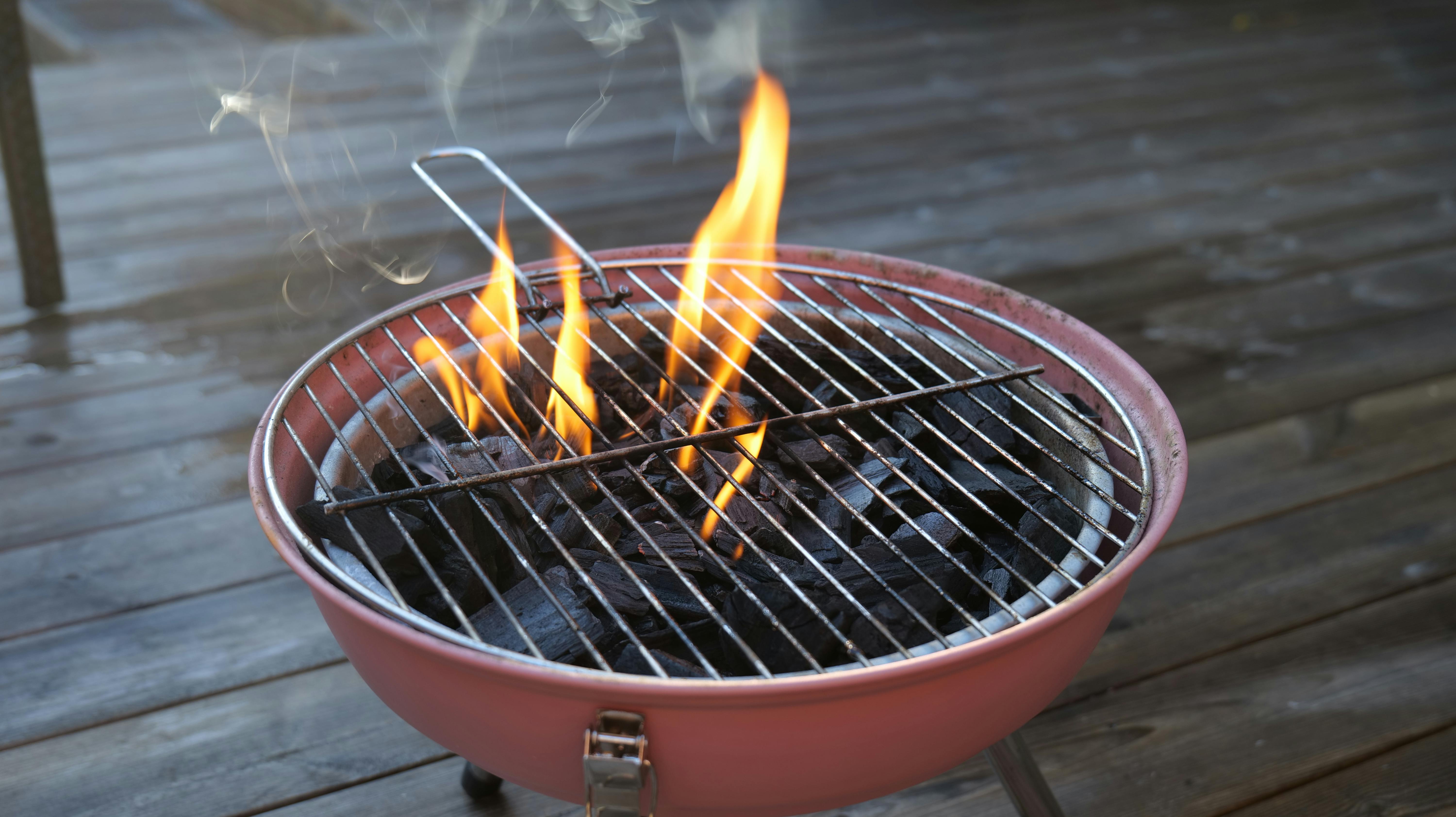 Kulgrill med flammer og trækul på en træterrasse