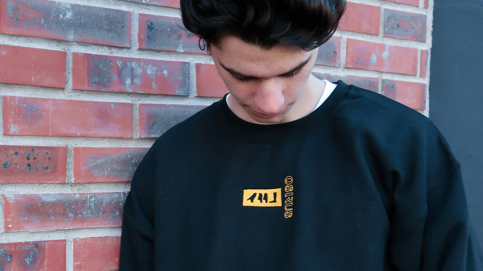 Mand i sort crewneck sweatshirt foran rød mur