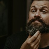 Mand der tjekker skæg og ansigt foran spejlet som cover til artikel om pincet og saks til mænd