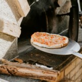 Pizza på metalspade ved træfyret pizzaovn