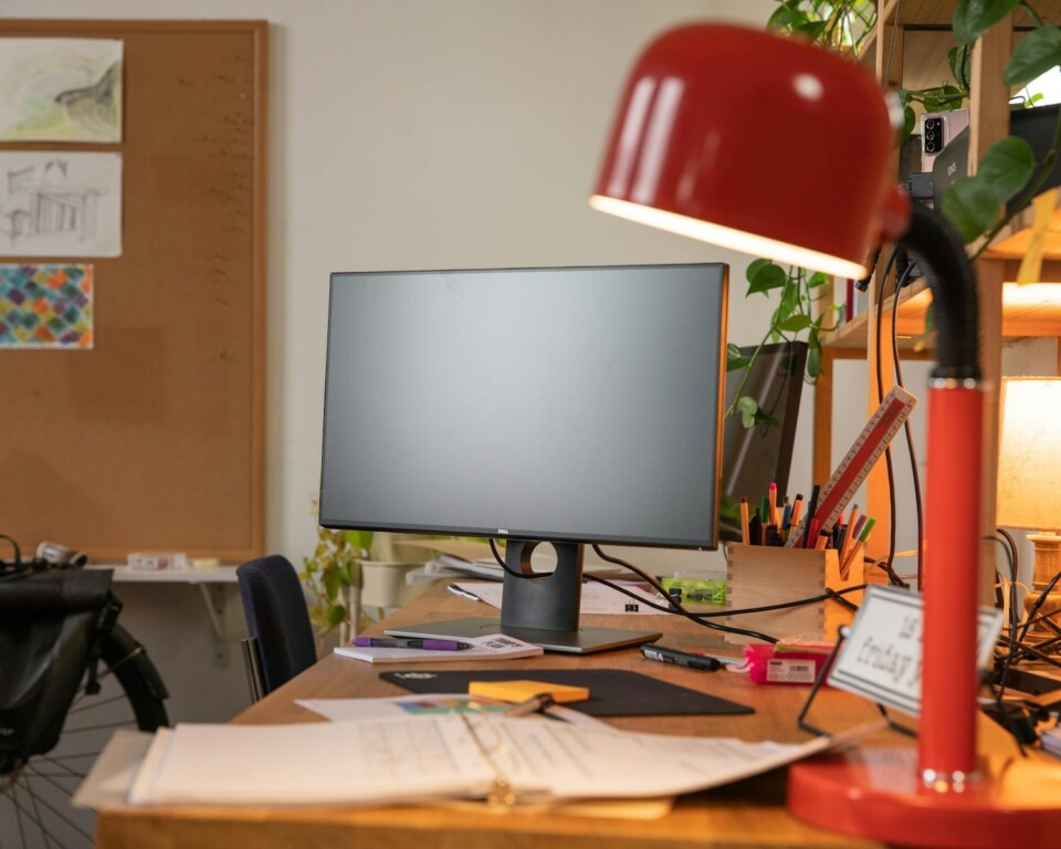 Hjemmekontor med rød skrivebordslampe, monitor og papirer på bordet