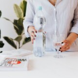 Person holder vandflaske og glas som del af en rolig sundhedsrutine