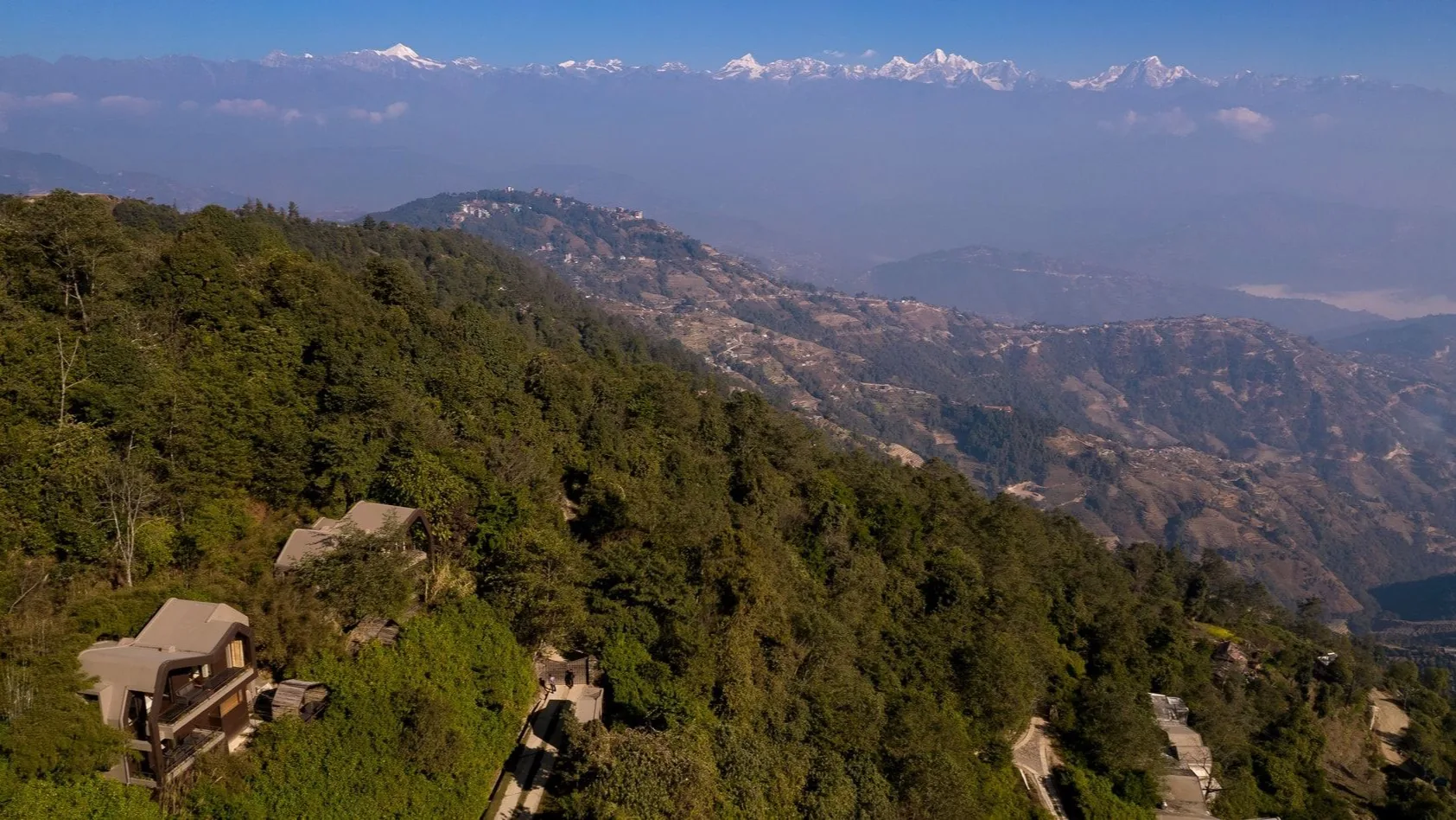 Bjerglodges i de grønne bakker med Himalaya i horisonten i Nepal