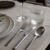 Dækket bord med rustfrit bestik, keramik, glas og linned