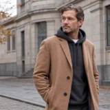 Voksen mand i mørkegrå hoodie og kamelfarvet frakke