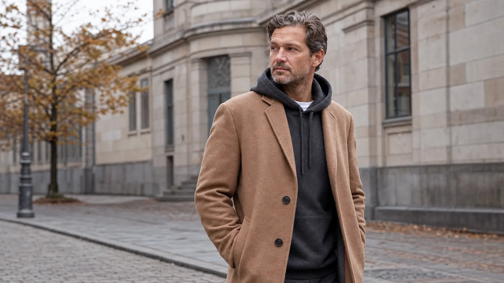 Voksen mand i mørkegrå hoodie og kamelfarvet frakke