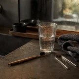 Tandbørste, glas vand og tungeskraber på en mørk badeværelsesbordplade