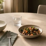 Yoghurt, bønnesalat, vand og en neutral tilskudsflaske på et lyst spisebord