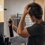 Mand styler håret med hårspray foran badeværelsesspejl