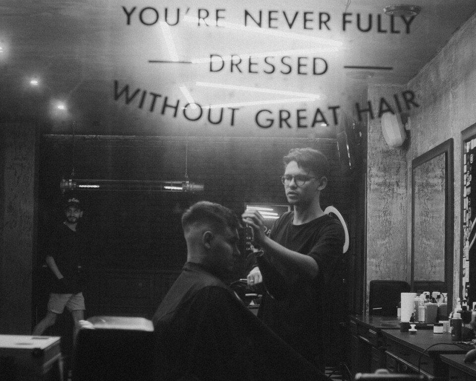 Barber styler hår i barbershop som cover til artikel om hårvand til mænd