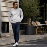 Mand i gråmeleret sweatshirt, mørke jeans og hvide sneakers foran en cafe