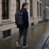 Mand med sort minimalistisk rygsæk på en våd københavnsk bygade
