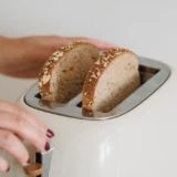 Skiver af fuldkornsbrød i en cremefarvet retrotoaster på et lyst køkkenbord