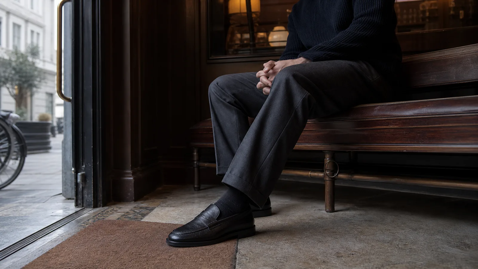 Mand i mørke uldbukser og sorte læderloafers ved indgangen til en klassisk café