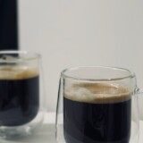 To dobbeltvæggede kaffeglas på et lyst bord