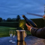 Champagneflaske og sløv sabel rettet mod en tom have ved skumring