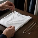 Hænder vælger mellem enkle sølvkæder ved en hvid T-shirt