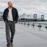 Joen går i grå relaxed fit jeans på en våd havnepromenade