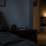 Analogt vækkeur på et mørkt natbord med telefonen til opladning uden for soveværelset