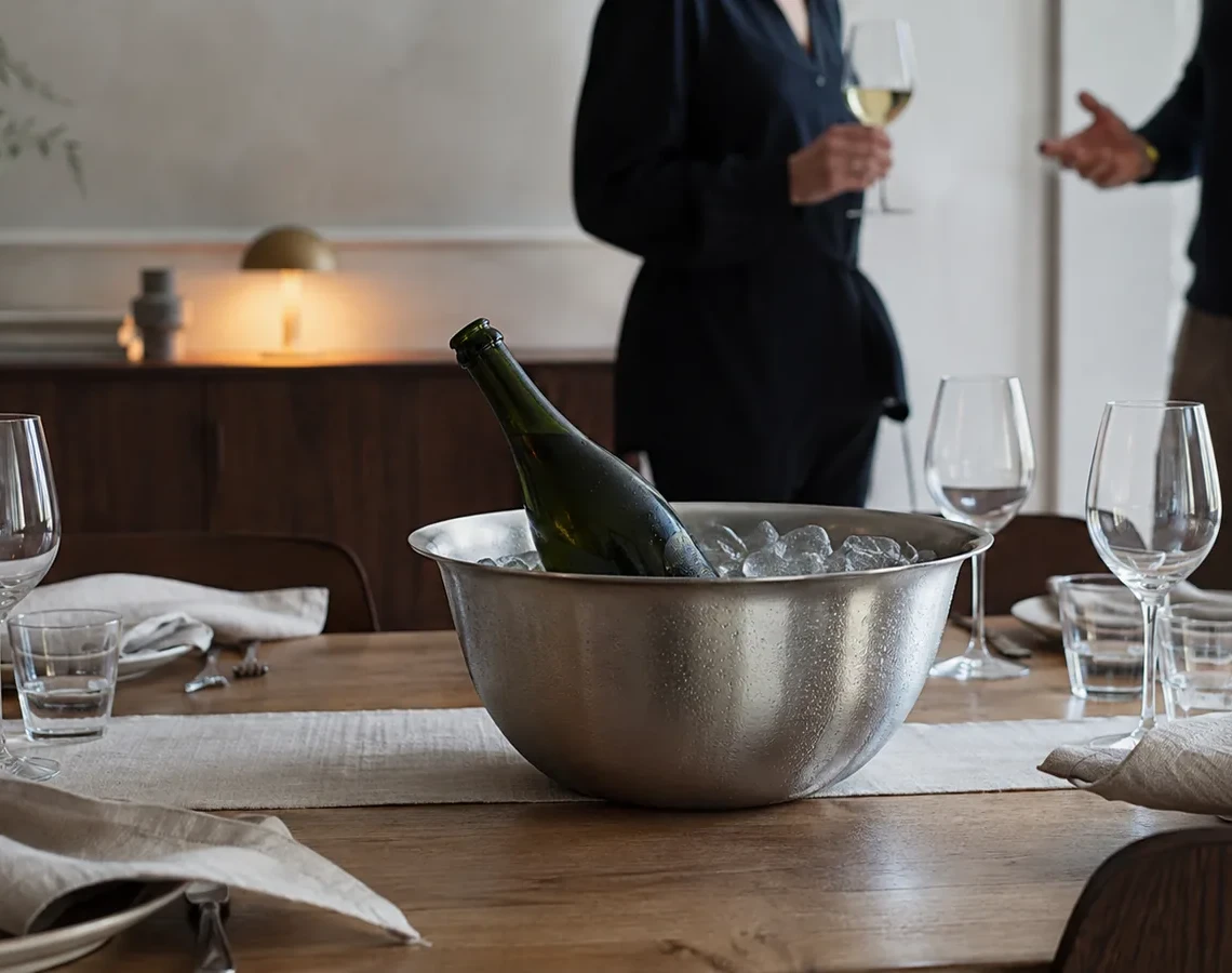 Champagneflaske i en stålskål med is og vand på et dækket bord, mens gæsterne ankommer