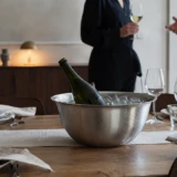 Champagneflaske i en stålskål med is og vand på et dækket bord, mens gæsterne ankommer