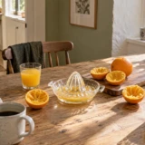 Citruspresser i glas, appelsinhalvdele og to glas juice på et lyst morgenbord