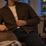 Brun cardigan over råhvid T-shirt ved middagsbordet, mens frakken hænger på stolen