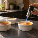 Gasbrænder karamelliserer sukker på tre portionsforme i et varmt køkken