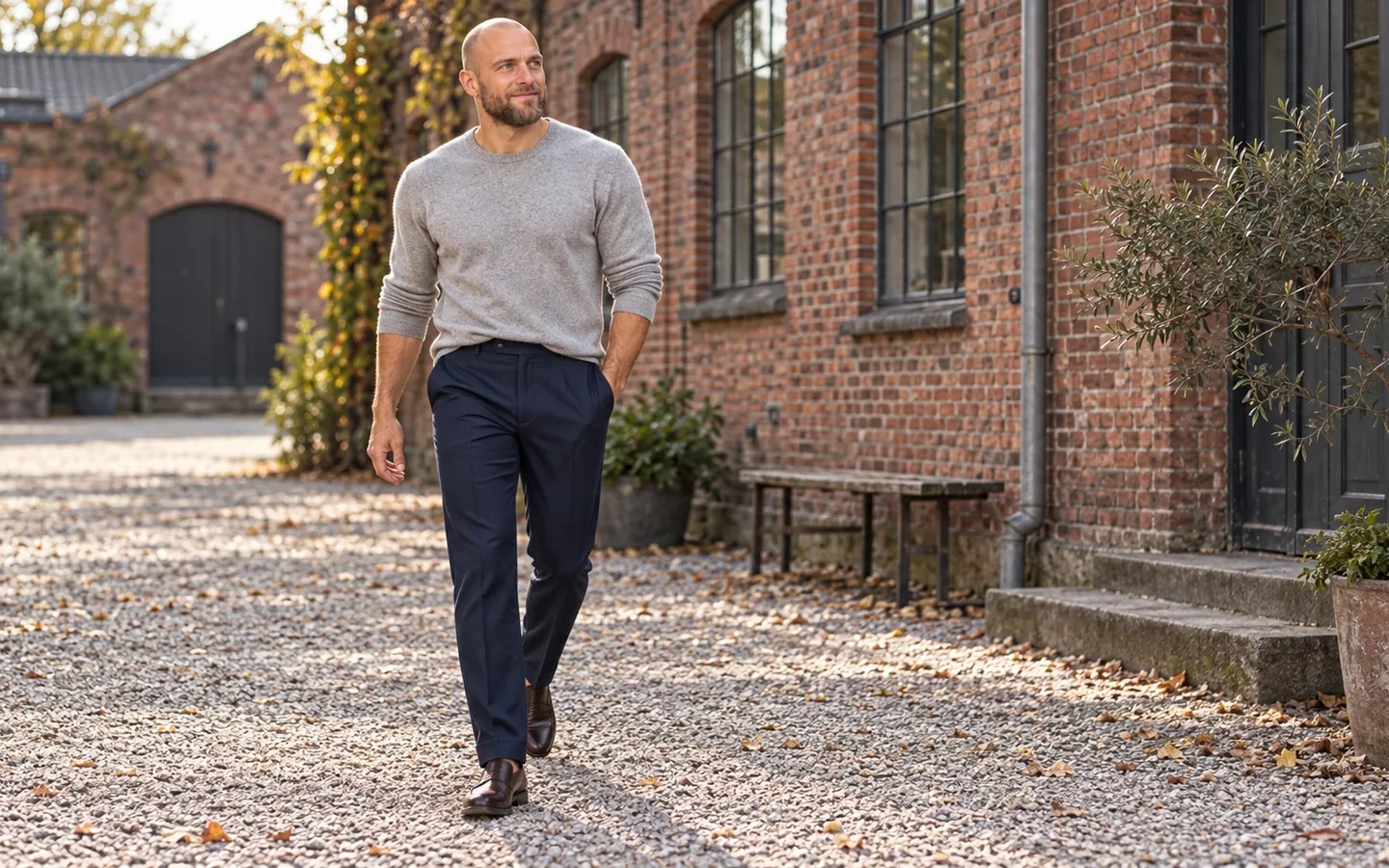 Joen i navy habitbukser og grå strik i en murstensgård
