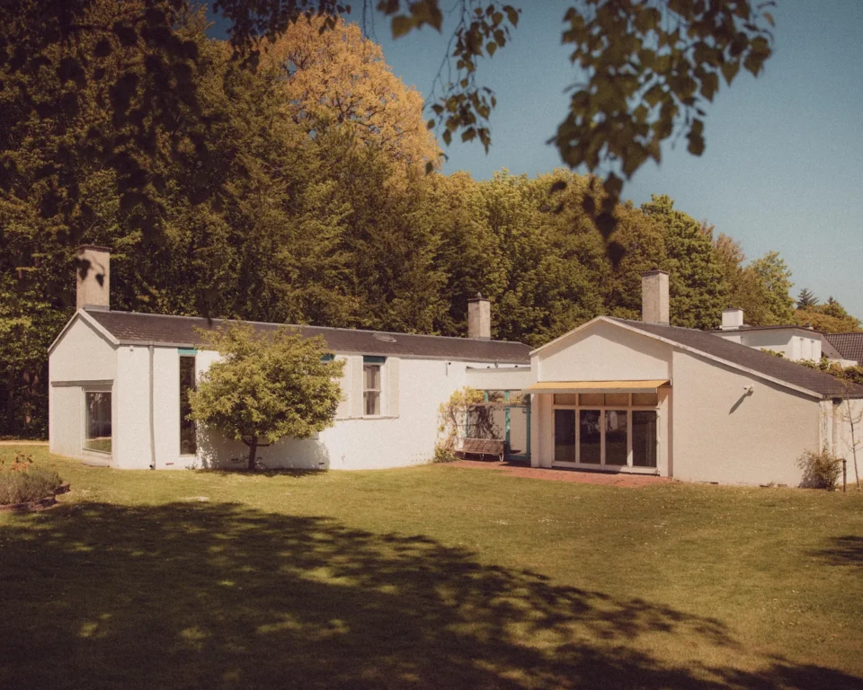 Finn Juhls hvide hus set fra haven med store vinduer og skov i baggrunden